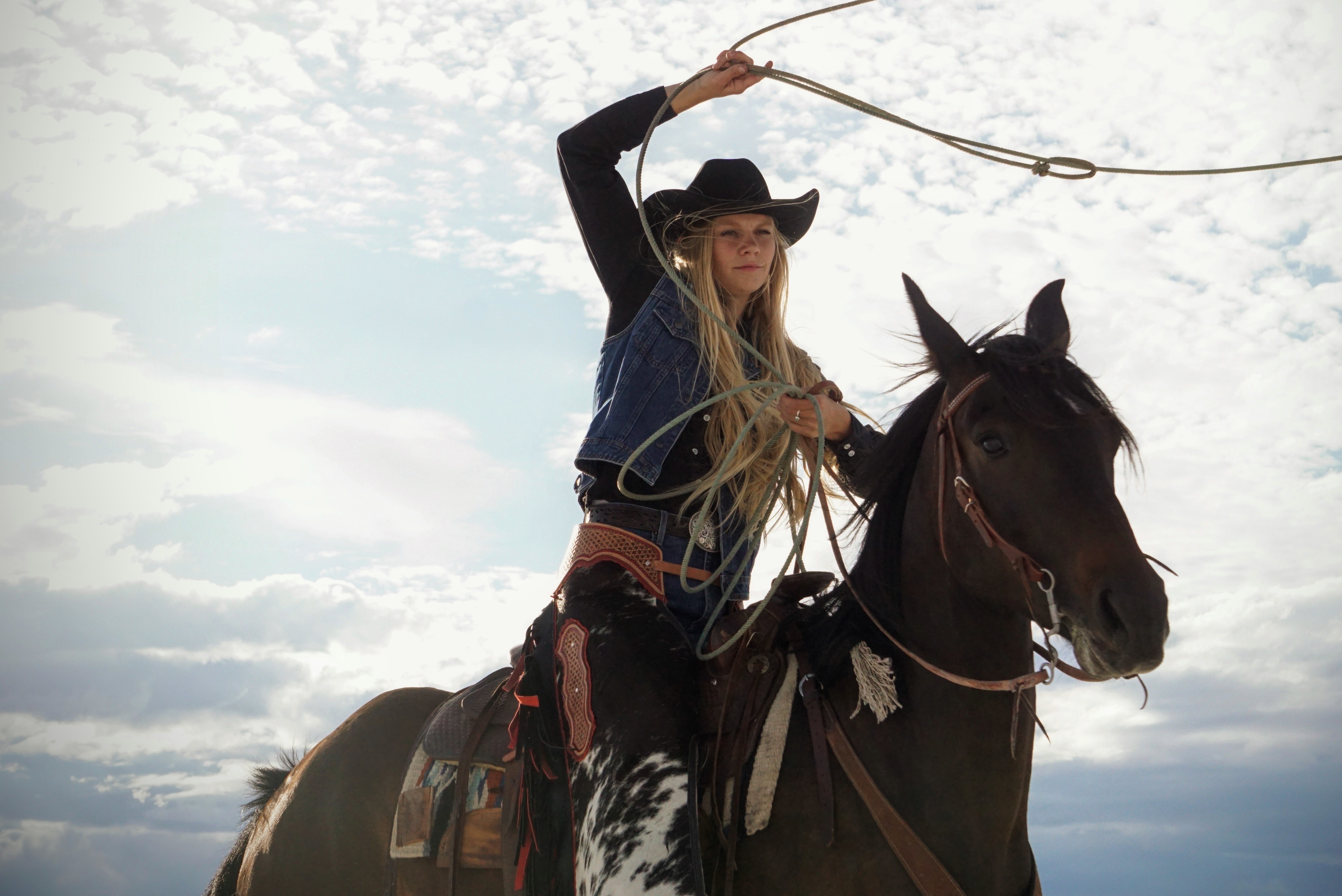 Lifestyle — Cowgirl on horseback swinging a lasso against a stormy sky