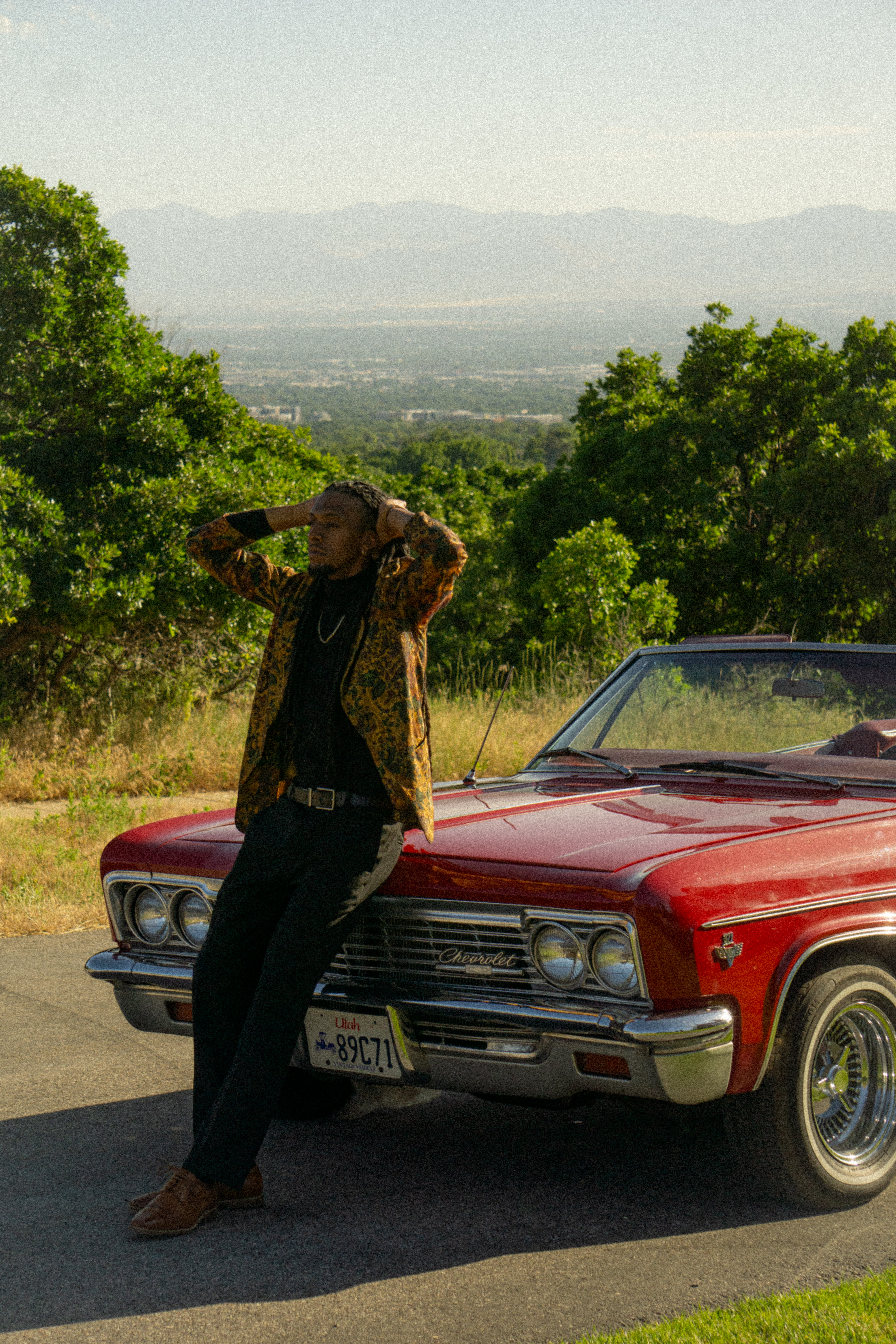 Portrait — Man leaning on a red Chevrolet with a mountain view